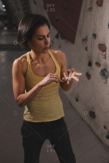 Young lady in sportswear fixing finger tape near wall with climbing holds in gym