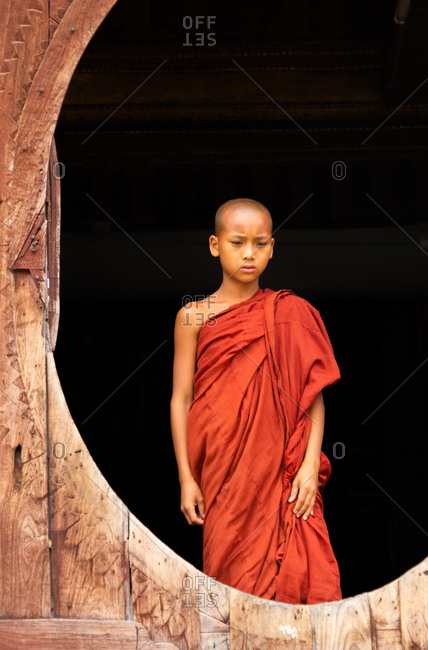 Mandalay, Myanmar - June, 25 2012: Bald ethnic boy in monk apparel standing inside shabby monastery building
