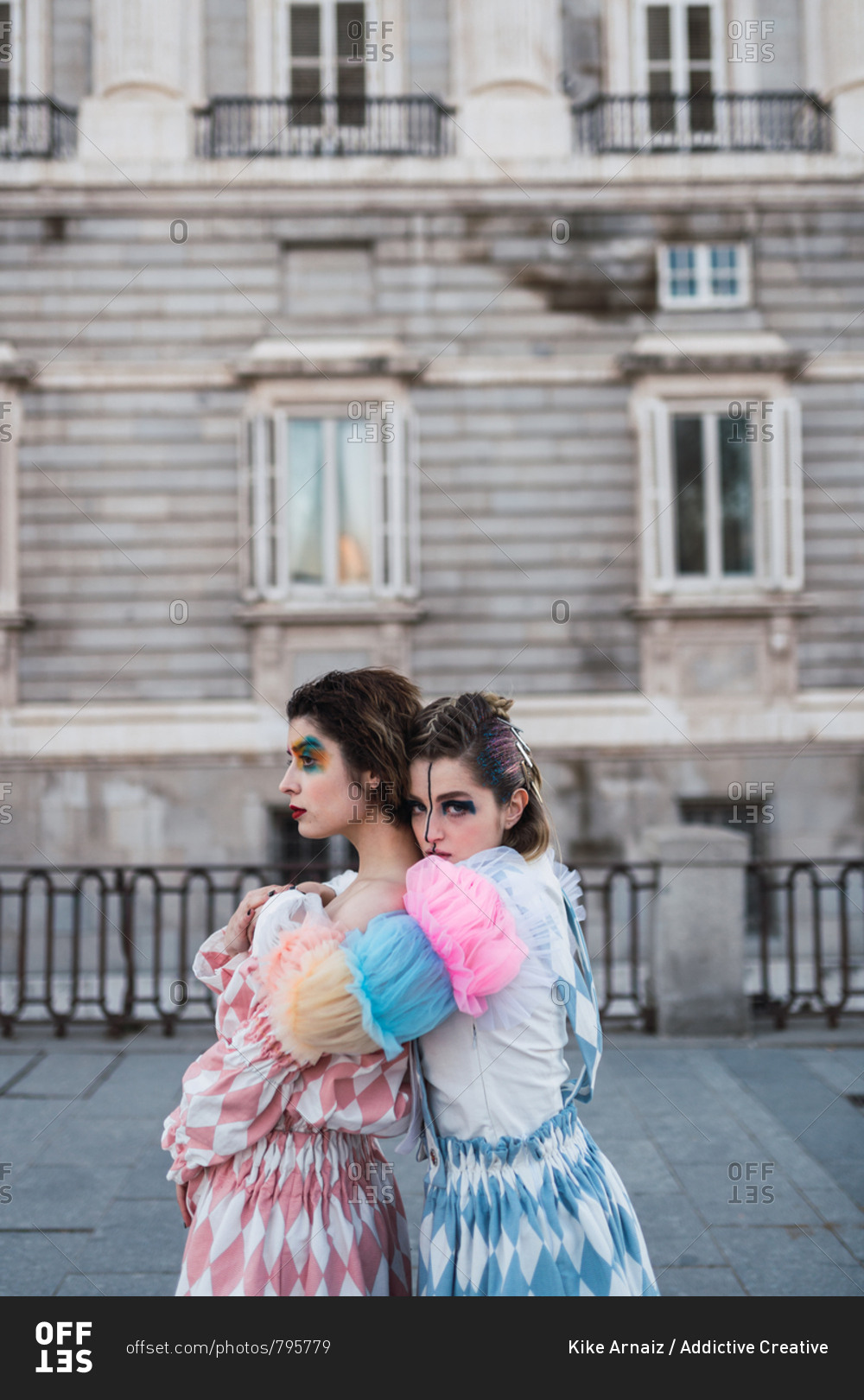 Side view of Two young women with theatrical makeup and unusual clothes performing and hugging on city street