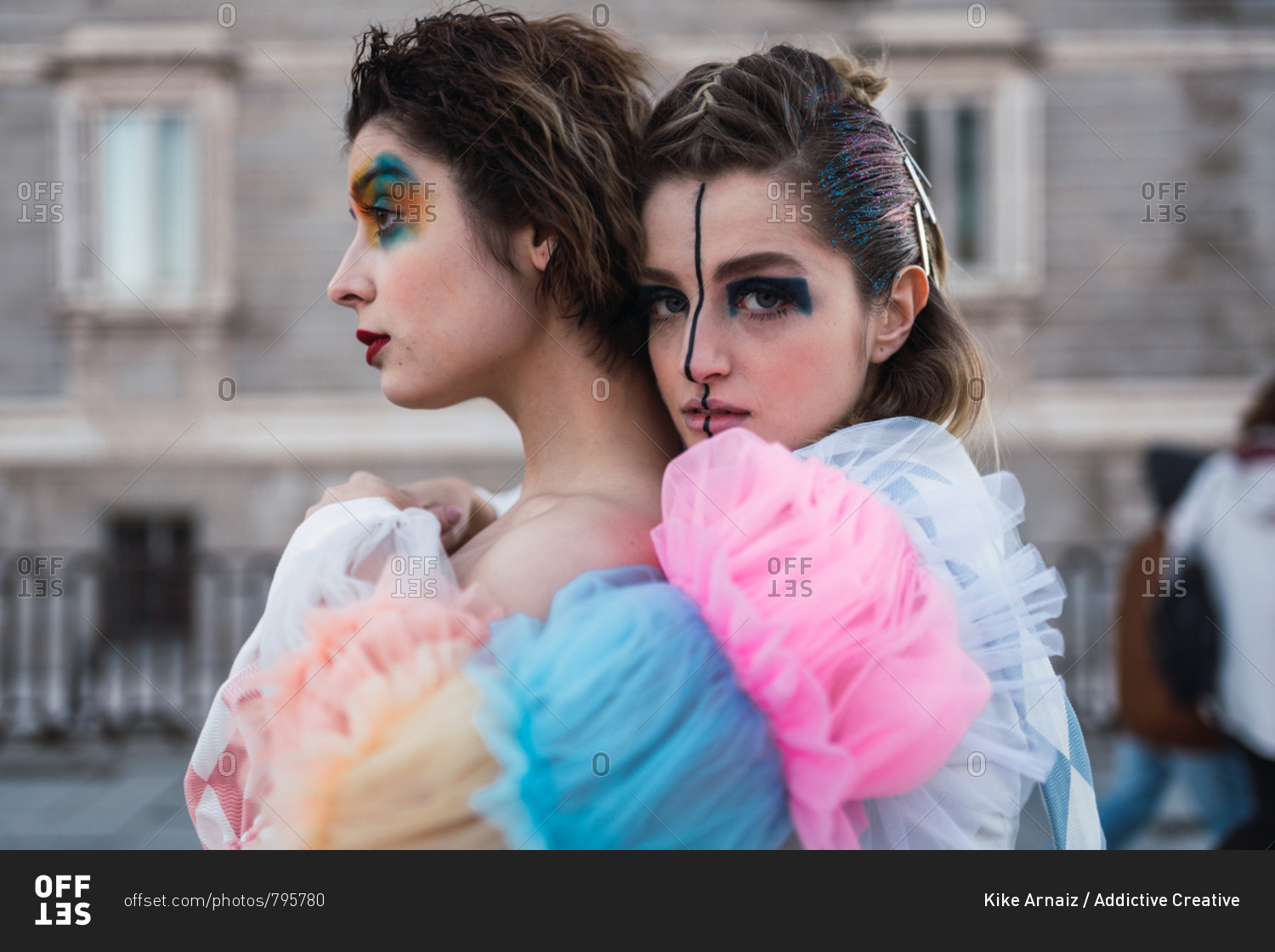 Side view of Two young women with theatrical makeup and unusual clothes performing and hugging on city street