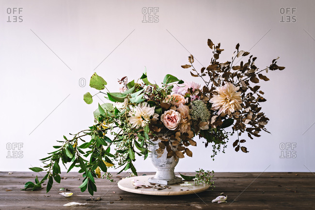 Concept of bouquet of dry and fresh roses, chrysanthemums and plant twigs in retro vase on wooden board on grey background