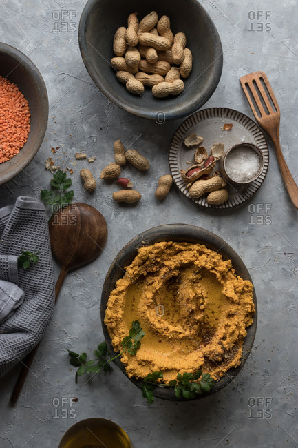 Bowl with delectable lentil hummus with carrot and fresh peanuts standing on gray plaster surface