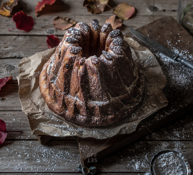 Fresh tasty Kugelhopf standing on parchment paper on weathered lumber tabletop near dry autumn leaves