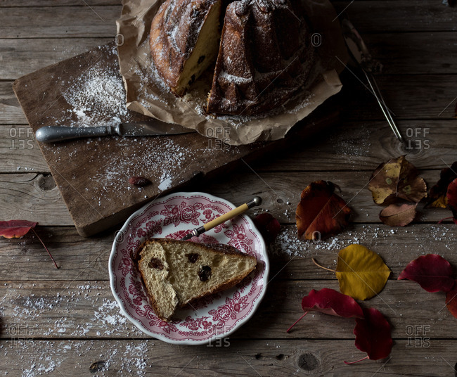 Delicate autumn leaves lying on shabby timber tabletop near plate and parchment paper with yummy fresh Kugelhopf