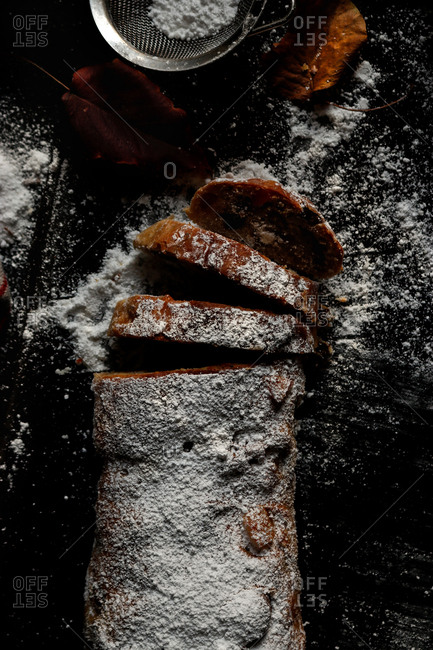 Pieces of delicious fresh Stollen covered with powdered sugar lying on dark tabletop