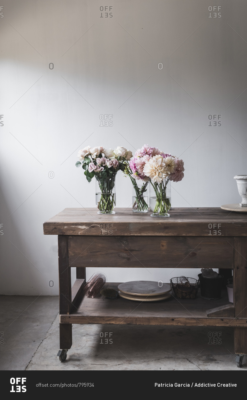 Wooden table with kitchenware and bouquets of fresh blooms in vases with water near white wall