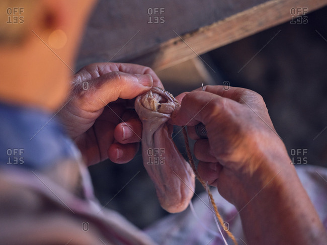 Unrecognizable senior male in apron sewing bag from fresh animal bowel