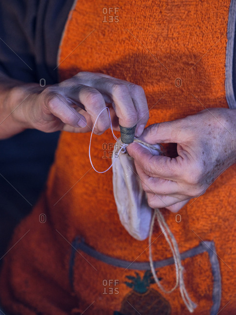 Unrecognizable senior female in apron sewing bag from fresh animal bowel