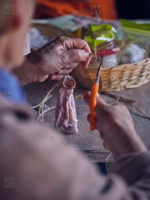 Unrecognizable elderly female using scissors to cut linen thread on empty animal guts over table