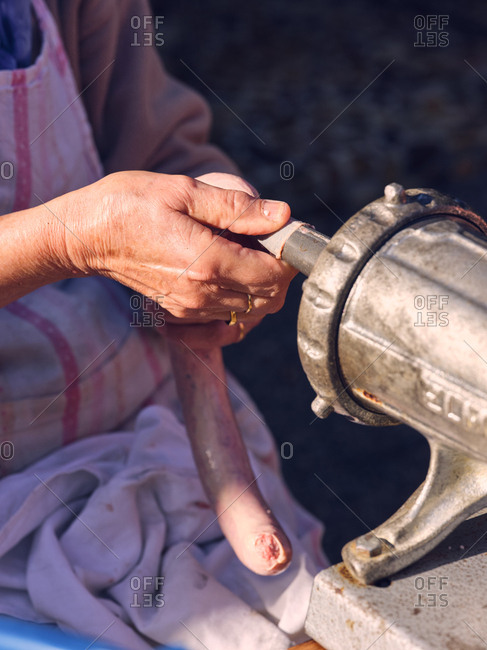 Unrecognizable elderly woman using metal machine to fill animal bowel with minced meat