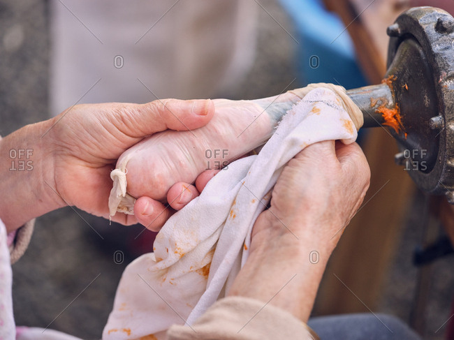 Unrecognizable elderly woman using metal machine to fill animal bowel with minced meat
