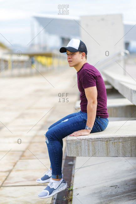 Side view of a teenager wearing casual attire while sitting on a bench outdoors and looking away