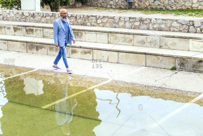 Side view of a hipster mature man wearing trendy attire while walking nest to a pond in a park