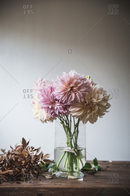 Wooden table with kitchenware and bouquet of fresh blooms in vase with water near white wall