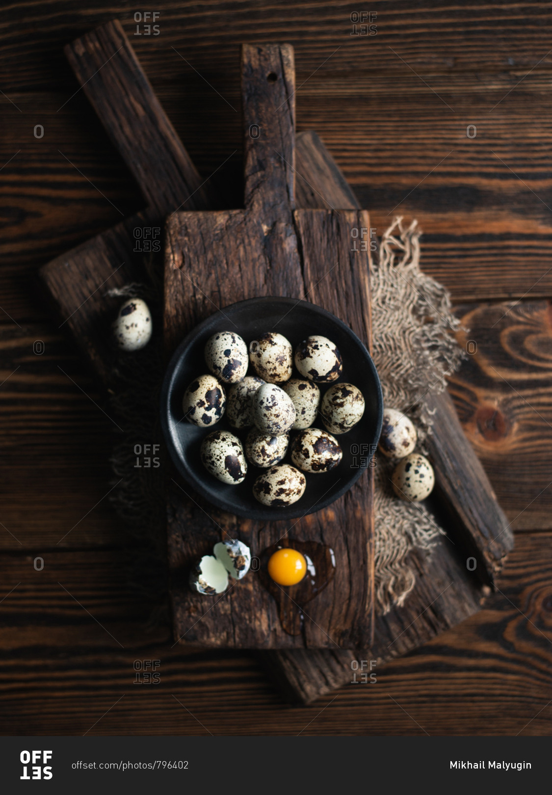 Quail eggs on dark ceramic plate over brown wooden background, view from above