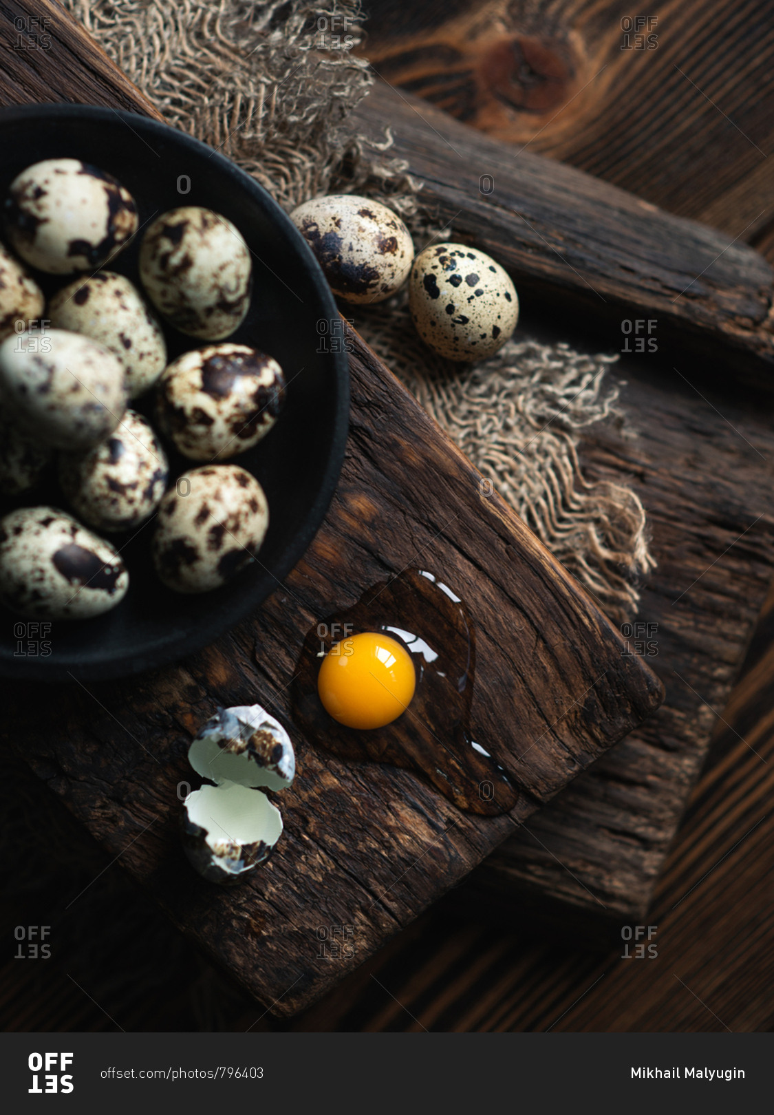 Quail eggs on dark ceramic plate over brown wooden background, view from above
