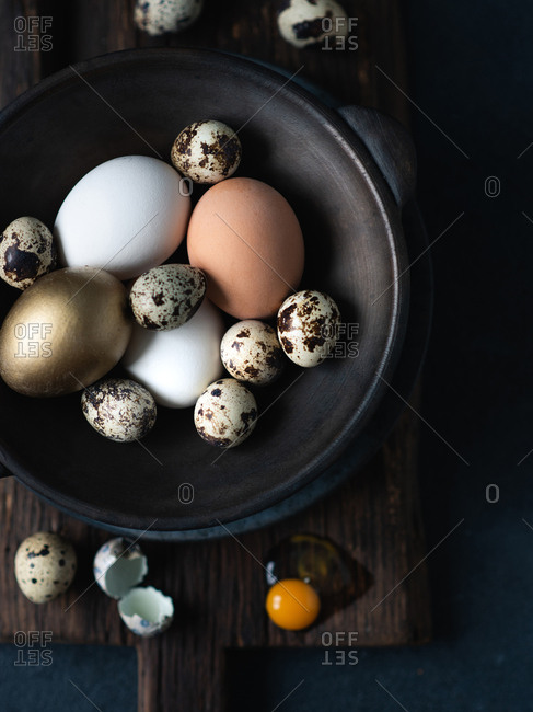 Easter eggs in dark ceramic bowl over dark background, view from above