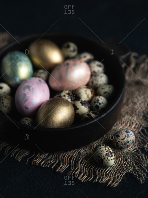 Colorful Easter eggs in dark ceramic bowl over dark background