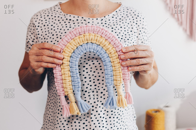 Female hands holding and displaying an authentic small multicolored pink, yellow and blue macrame.