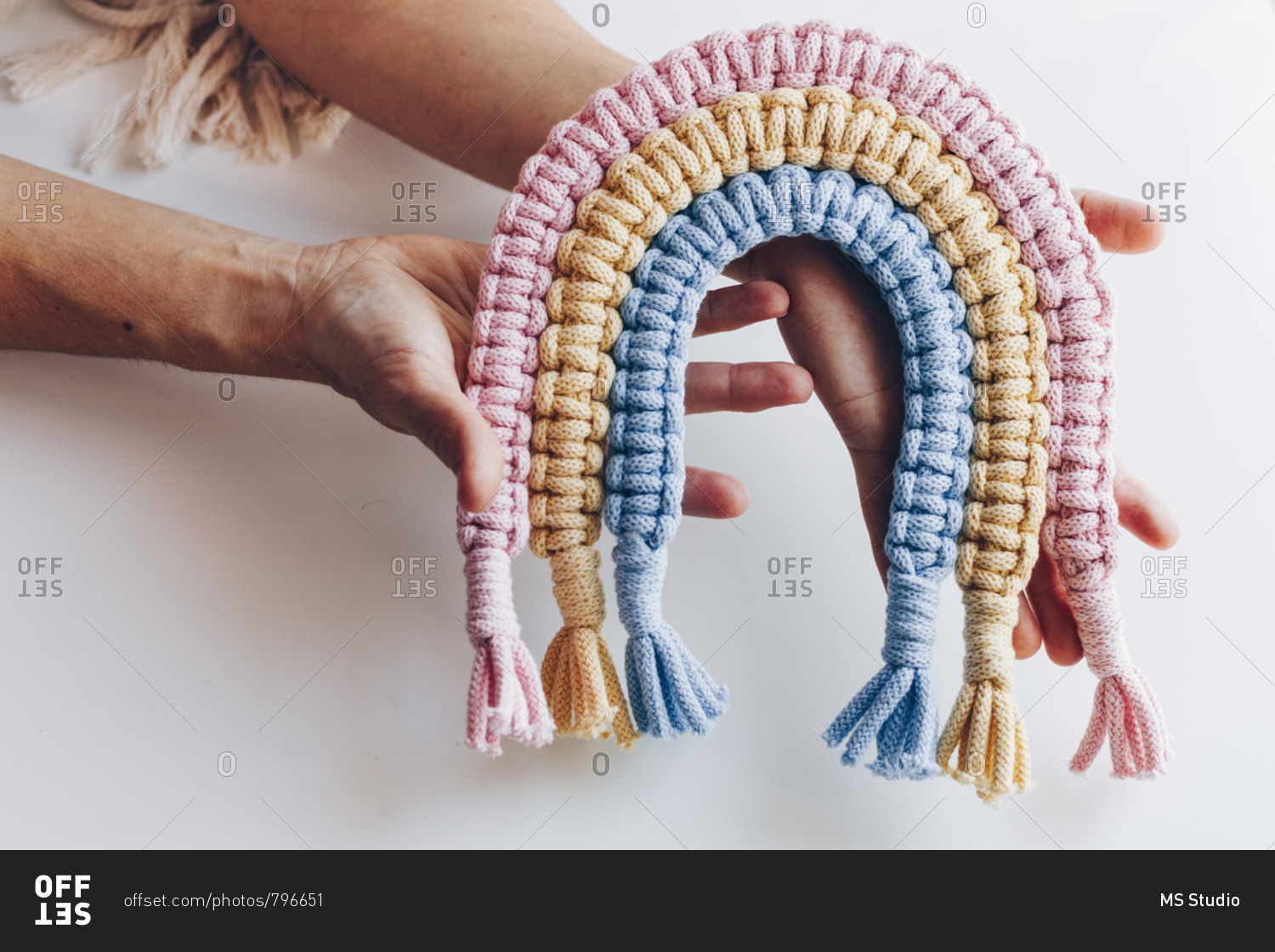 Top view close up of female hands displaying a multicolored pink, yellow and blue macrame decor.