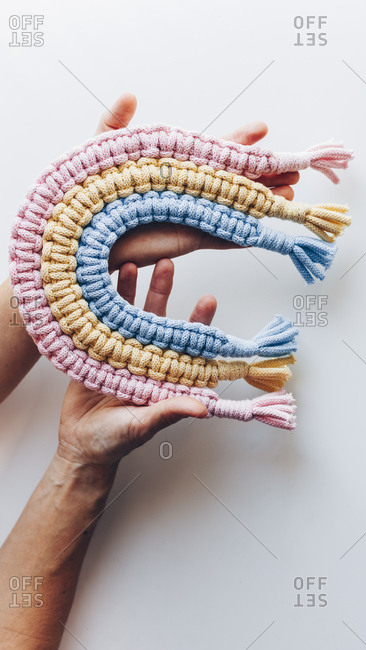 Top view closeup of female hands displaying a multicolored pink, yellow and blue macrame decor.