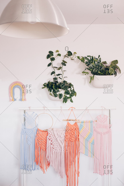 Multiple multicolored macrame's displayed on a pipe hanger in a modern home workshop. Vertical shot.