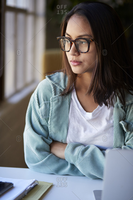 Millennial woman sitting at a desk in a casual office looking out of the window, vertical, close up