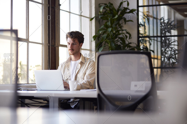 Millennial male blogger working at a desk in an office, selective focus