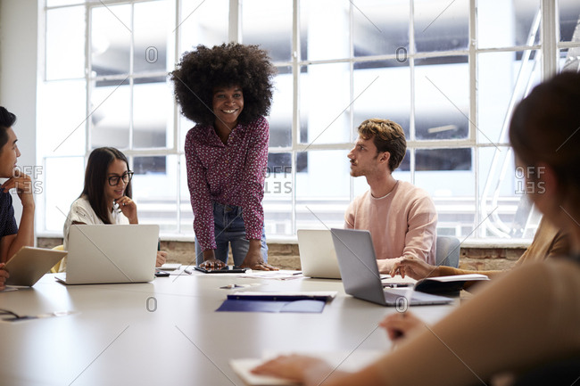 Female manager stands listening to colleagues sitting at a table in a meeting room, selective focus