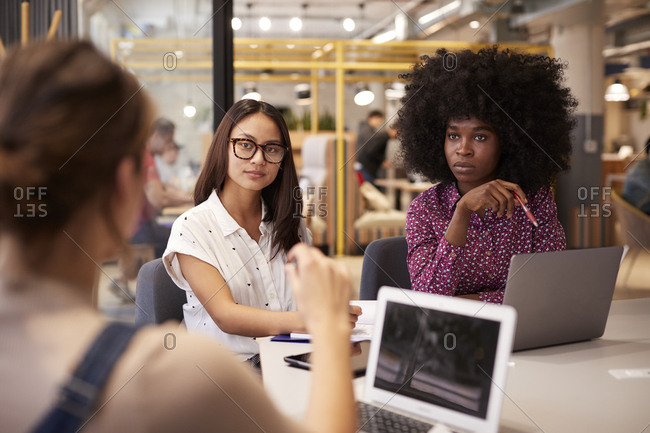 Three female  millennial creatives in discussion in a casual office meeting room, selective focus