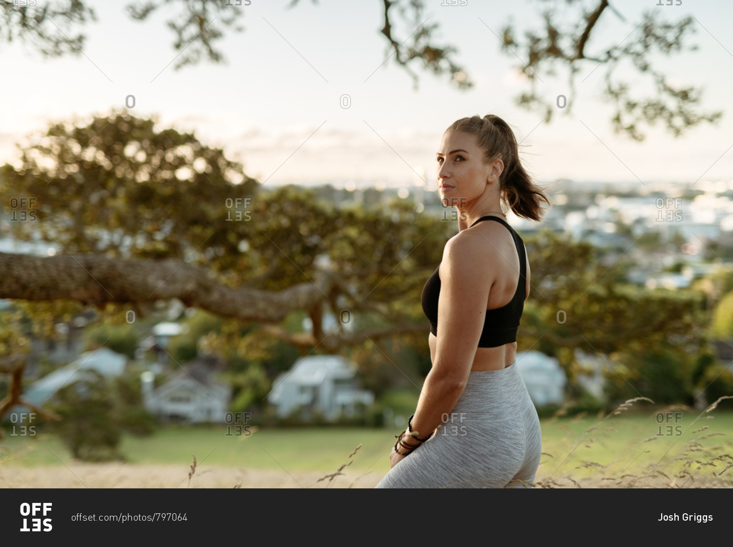 Young woman in workout clothes overlooking city from hilltop