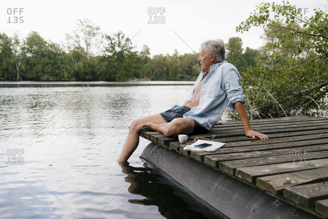 Senior man sitting on jetty at a lake
