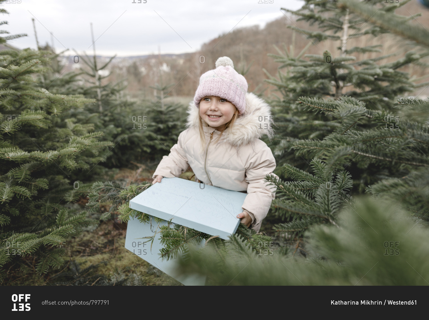 Happy girl carrying gift box on a Christmas tree plantation