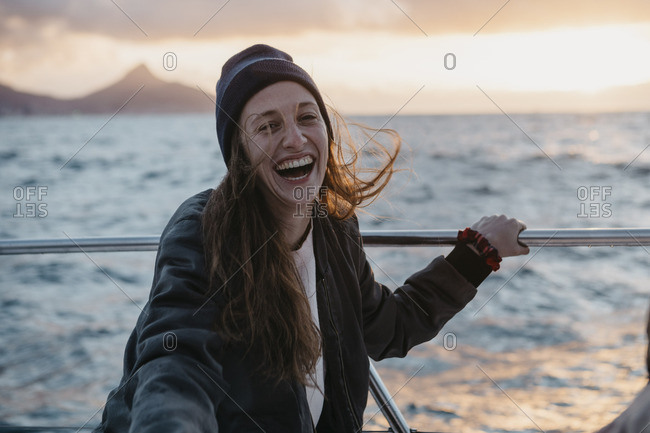 South Africa- young woman with woolly hat laughing during boat trip at sunset