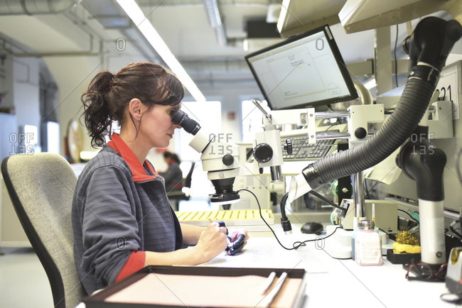 Woman using a microscope for the quality control in the manufacturing of circuit boards for the electronics industry