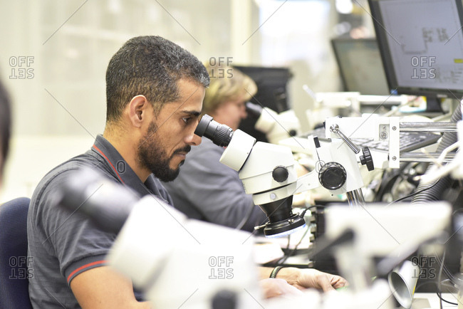 Man using a microscope for the quality control in the manufacturing of circuit boards for the electronics industry