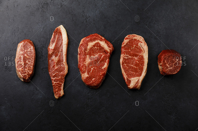 Variety of Raw Black Angus Prime meat steaks Top Blade,  Top sirloin cap, Rib Eye, Striploin, Tenderloin fillet Mignon on dark background