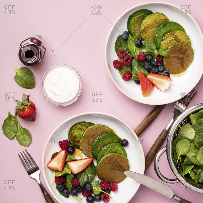 Spinach pancakes with fruits and vegetables on pink background, flat lay