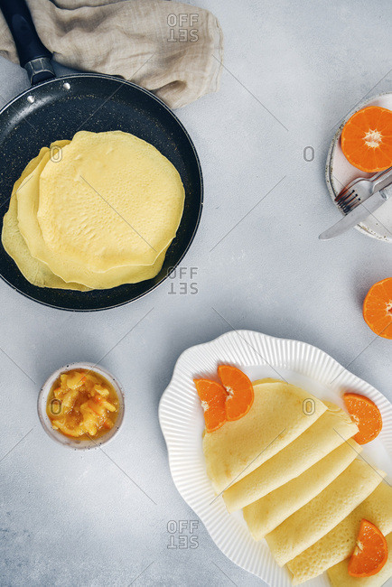 Gluten free crepes in a non stick pan and in a white oval plate garnished with orange slices, accompanied by orange jam.