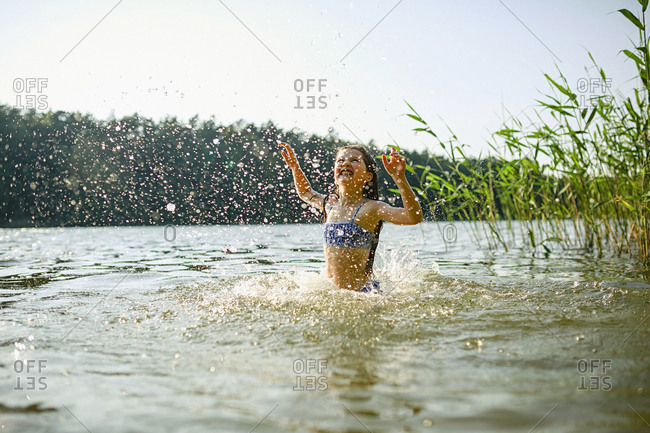 Playful girl splashing, swimming in sunny summer lake
