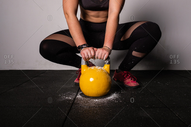 athletic young concentrated woman in sportswear upping kettle bell in gym