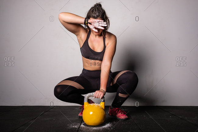 athletic young concentrated woman in sportswear upping kettle bell in gym