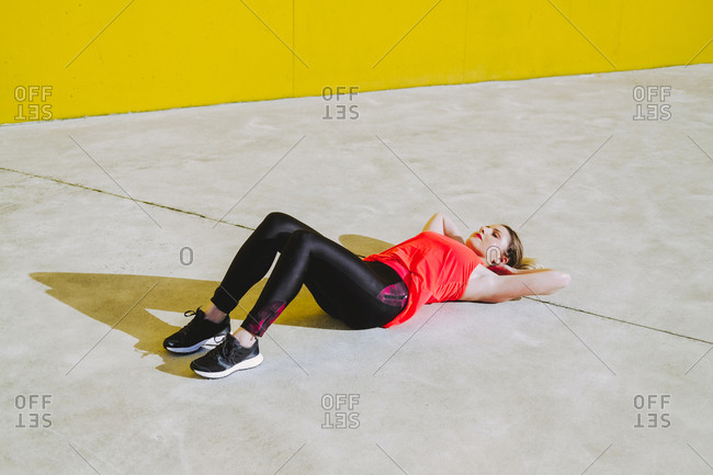 Young lady in sportswear doing sit ups exercises on floor near yellow wall
