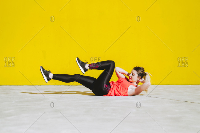 Young lady in sportswear doing sit ups exercises on floor near yellow wall