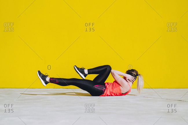 Young lady in sportswear doing sit ups exercises on floor near yellow wall