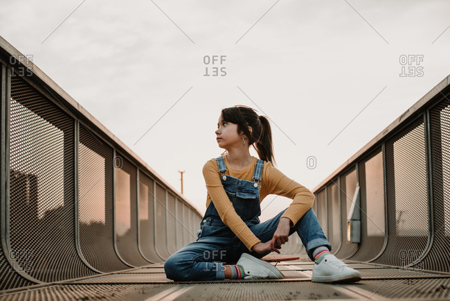Girl sitting on skateboard on walkway