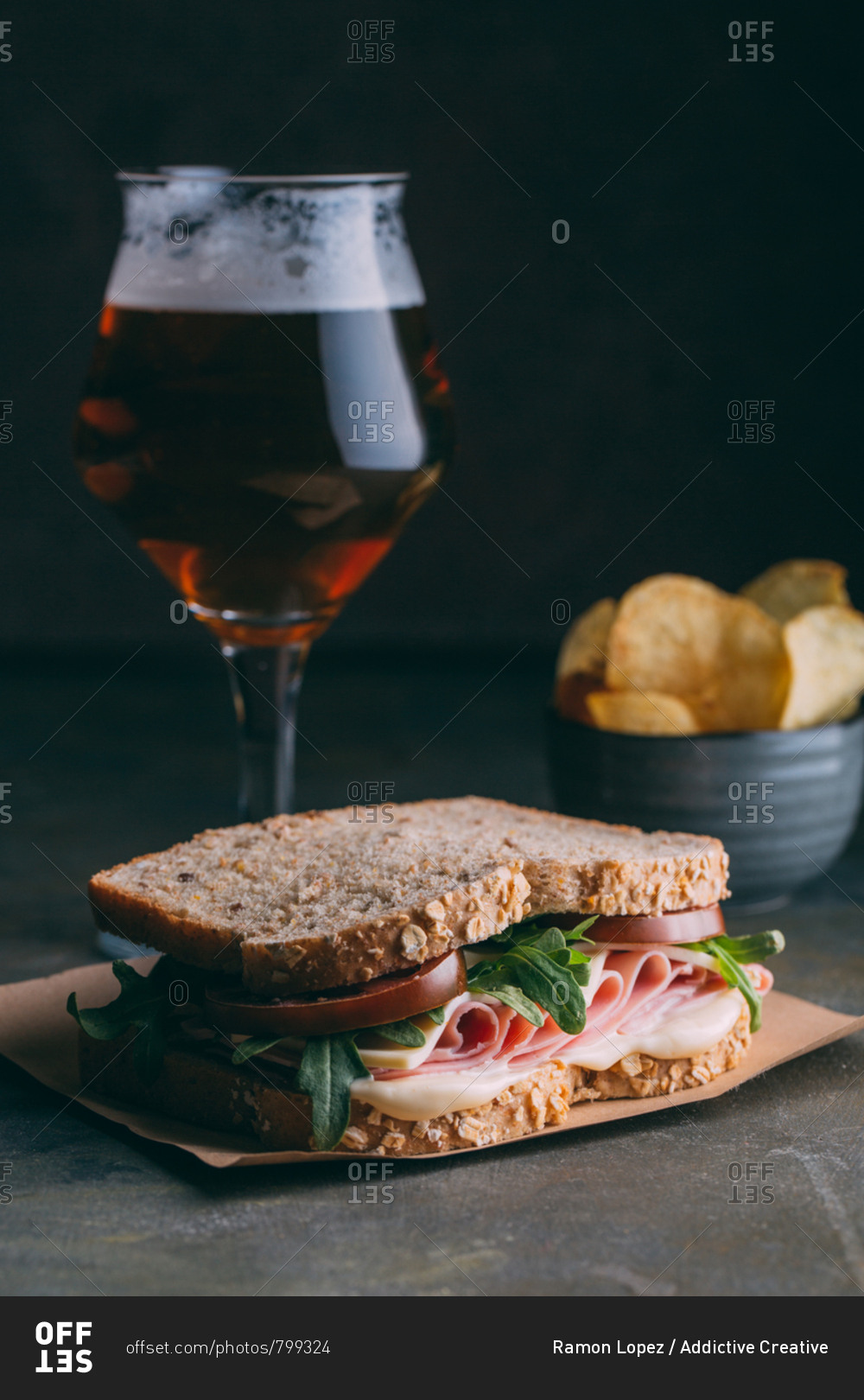 Delicious sandwich with ham, cheese, lettuce and tomato with a glass of beer and chips on dark and grunge background