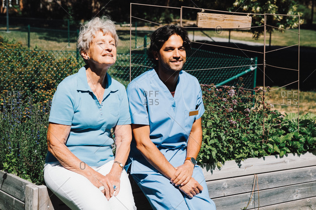 Smiling senior woman sitting with male nurse on planter at back yard