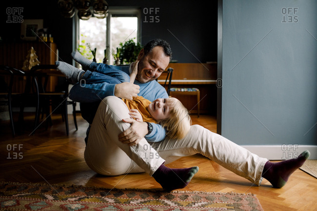 Full length of happy playful father carrying daughter while sitting on hardwood floor at home