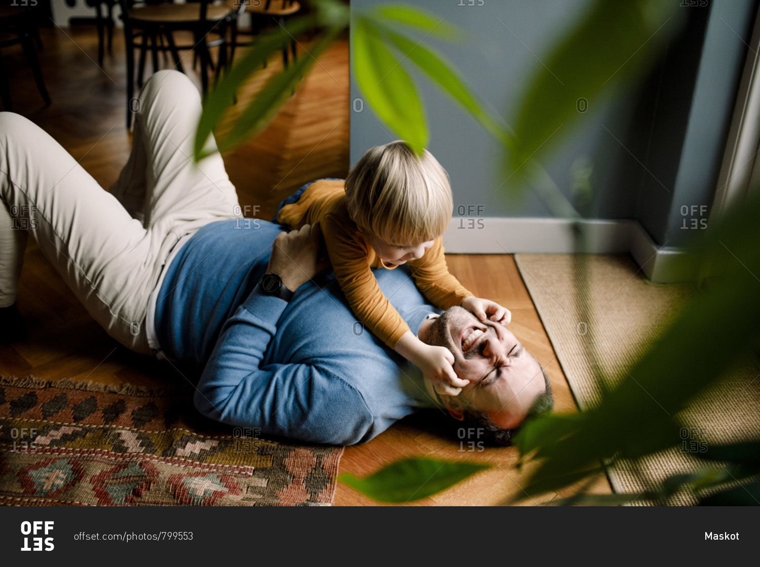 Playful daughter pinching cheerful father\'s cheeks on floor at home